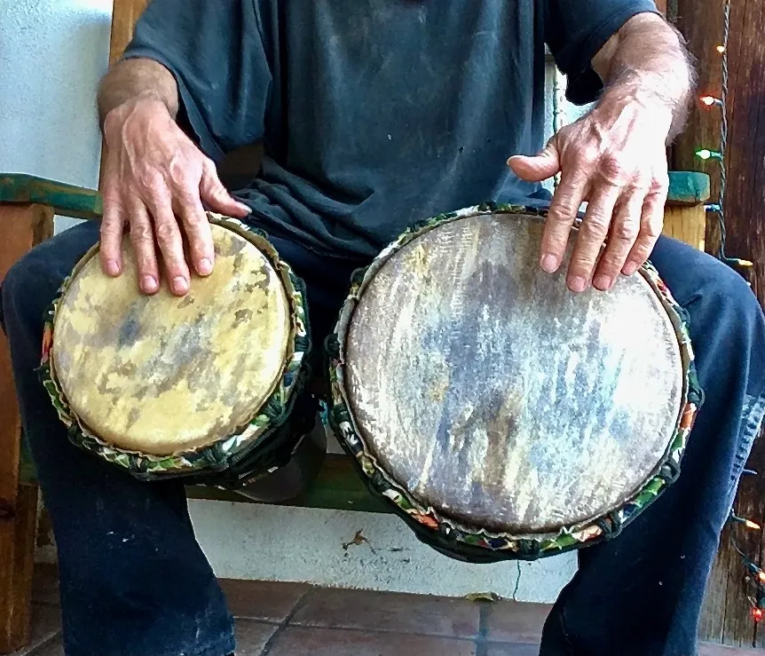 A man sitting on a bench playing two African harps, called Ilimba.