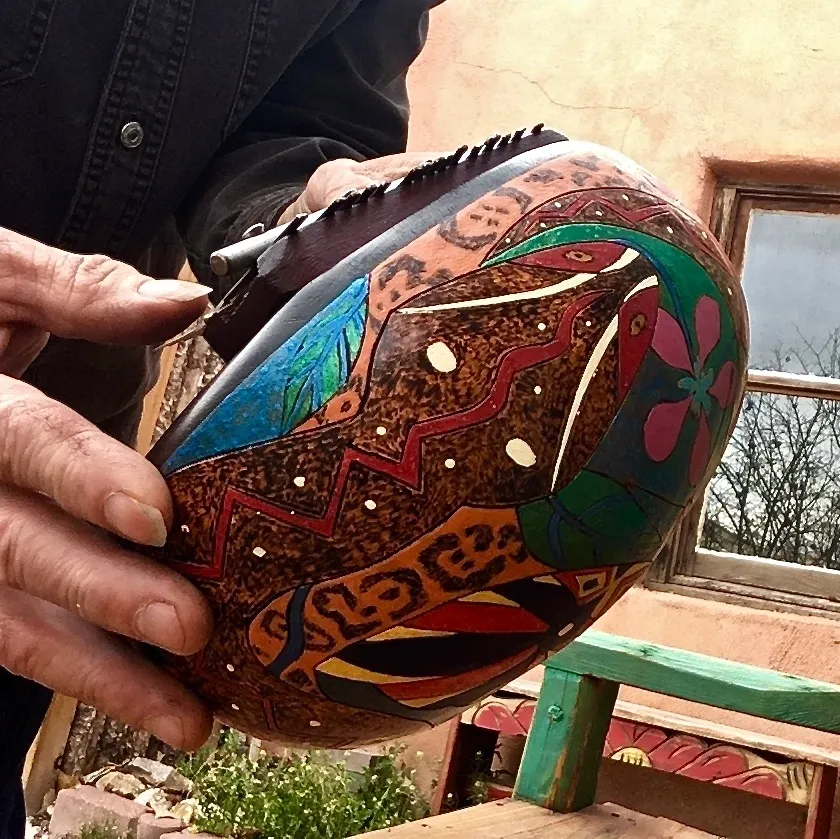 A man holding a Ngoma, a traditional African wooden ball adorned with colorful designs.