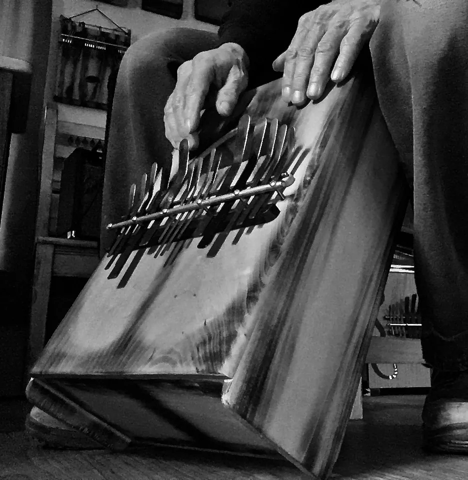 A black and white photo of a man playing a wooden box-like instrument.