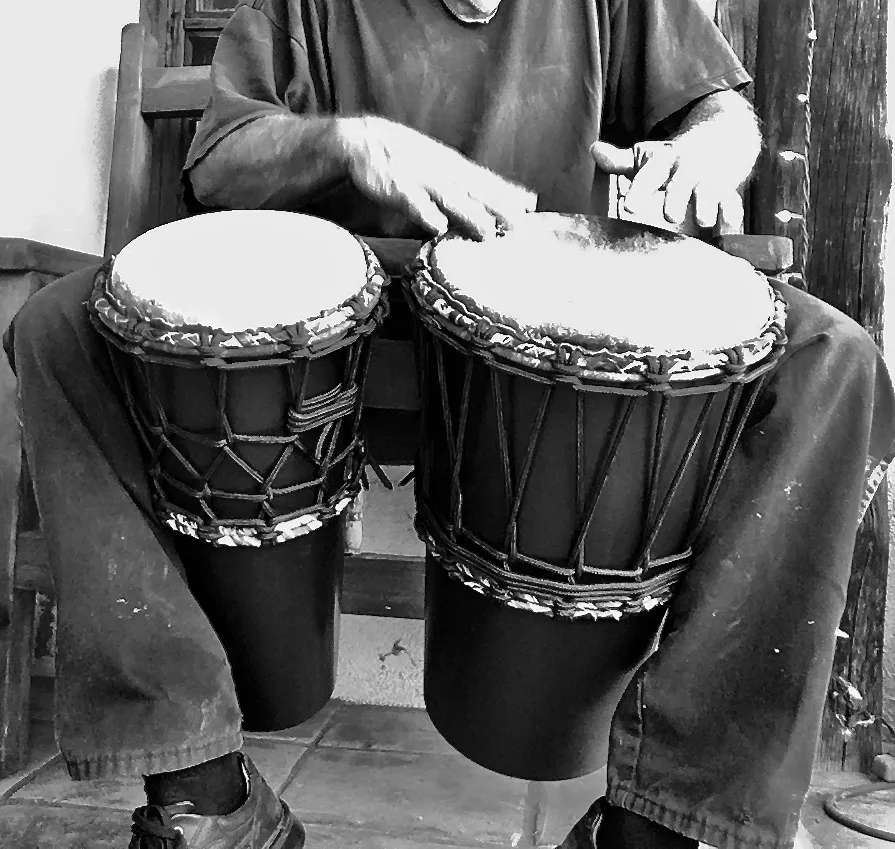 Black and white photo of a man playing a djembe, an African percussion instrument.