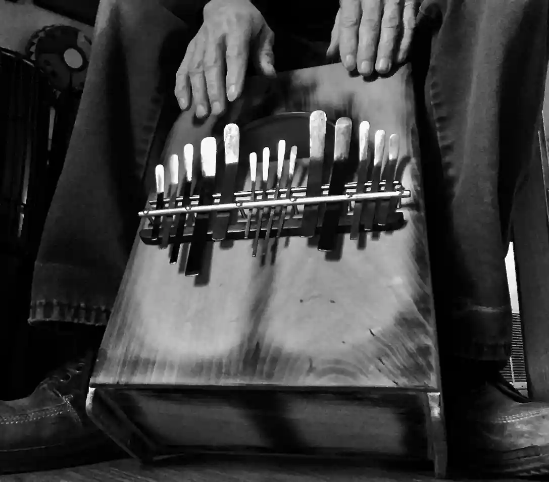 A black and white photo of a person holding a box of knives next to an African drum.