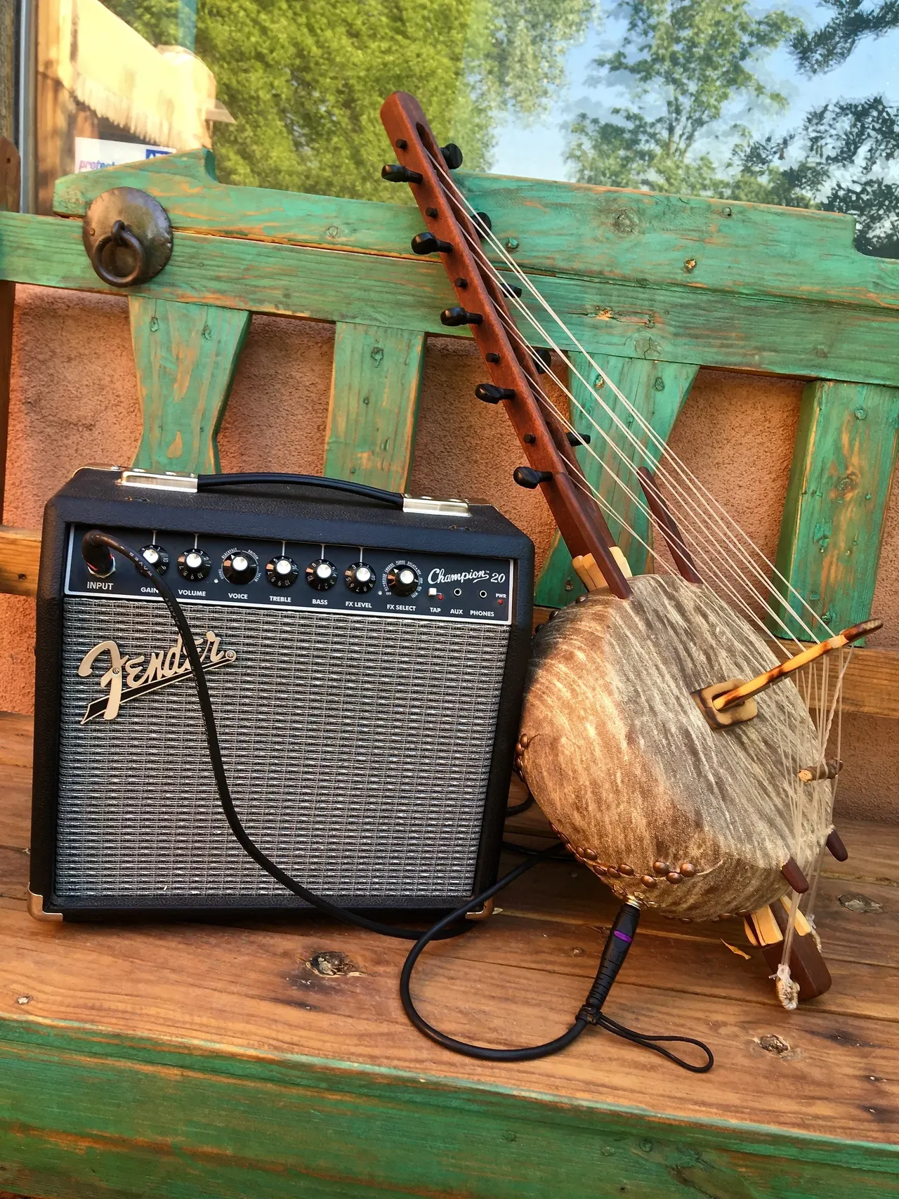 On a wooden bench, there is a harmonious combination of an Ngoma guitar amplifier and a traditional African harp.