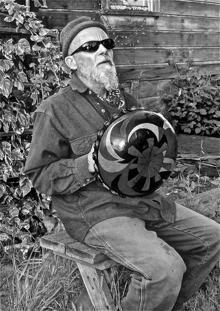 A man of African descent sitting on a bench, gently holding an Ilimba bowl.