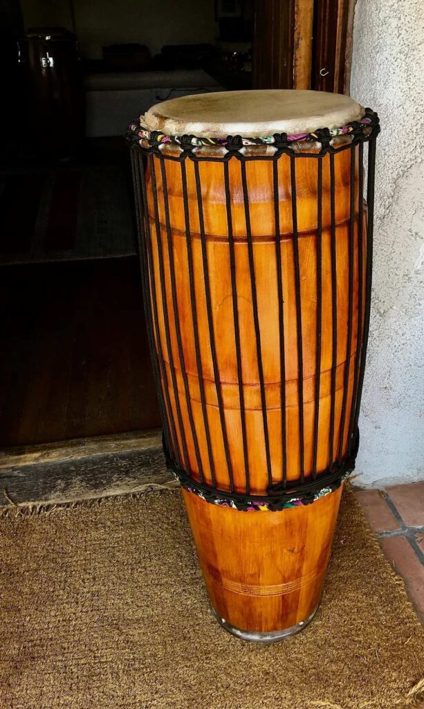 A wooden djembe, called Kongoma, sitting on a floor in front of a door.