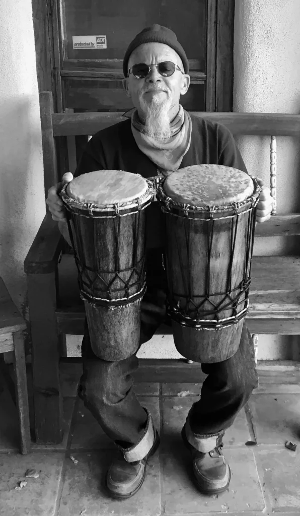 A man sitting on a bench with two djembes, showcasing his African harps.