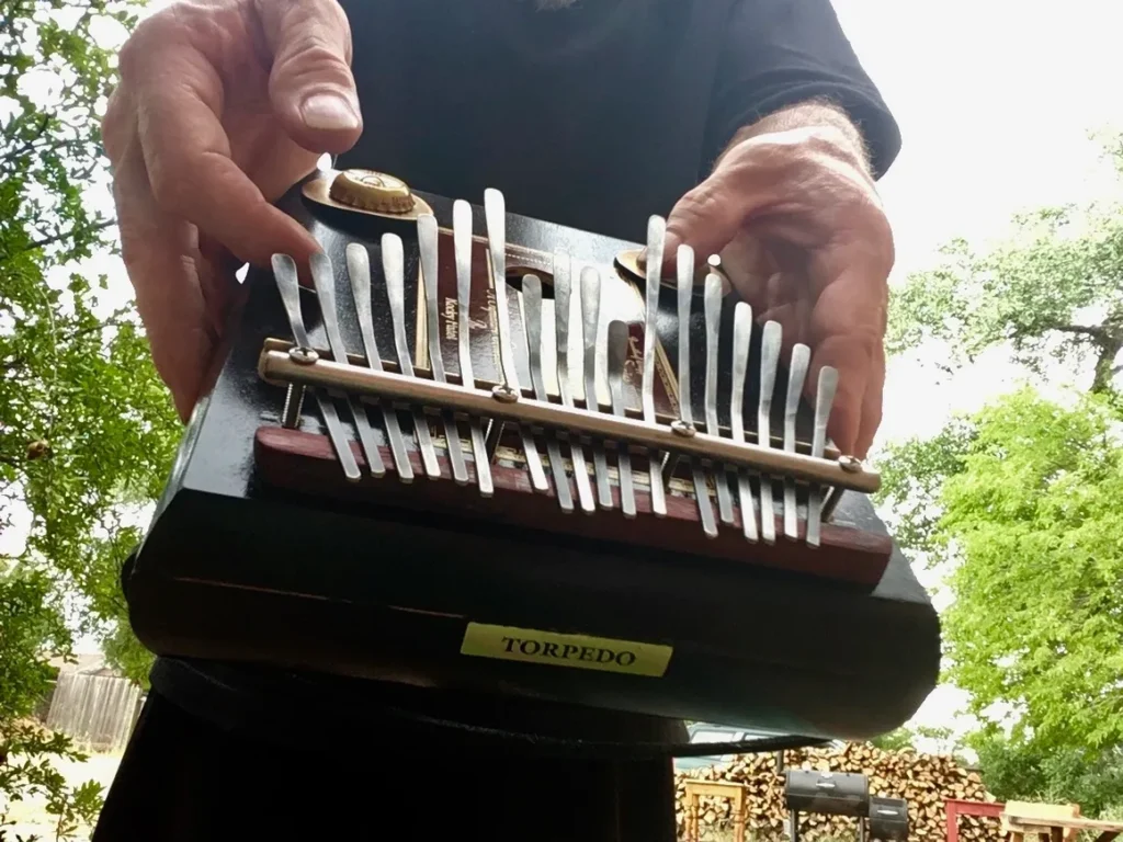 A man is holding up an accordion in a wooded area, playing African music.