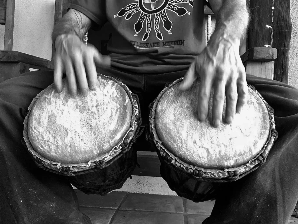 Black and white photo of a man playing a djembe, an African percussion instrument.