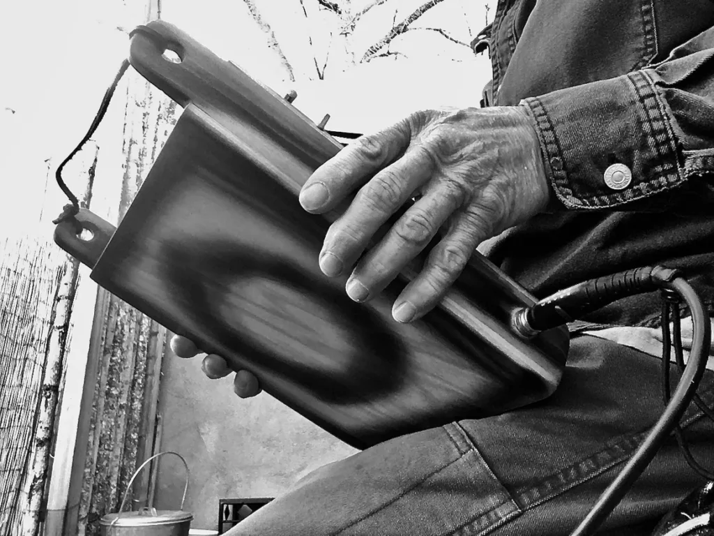 A man holding a laptop in his hands while playing gourd instruments.