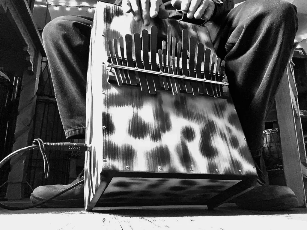 Black and white photo of a man playing an accordion alongside an African drum.