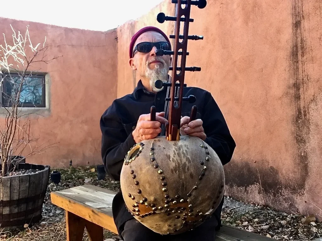 A man sitting on a bench, playing a Ngoma, a large wooden instrument used in African music.