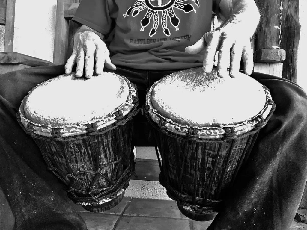 A man sitting on a bench with two djembes, showcasing the vibrant rhythms of African percussion.