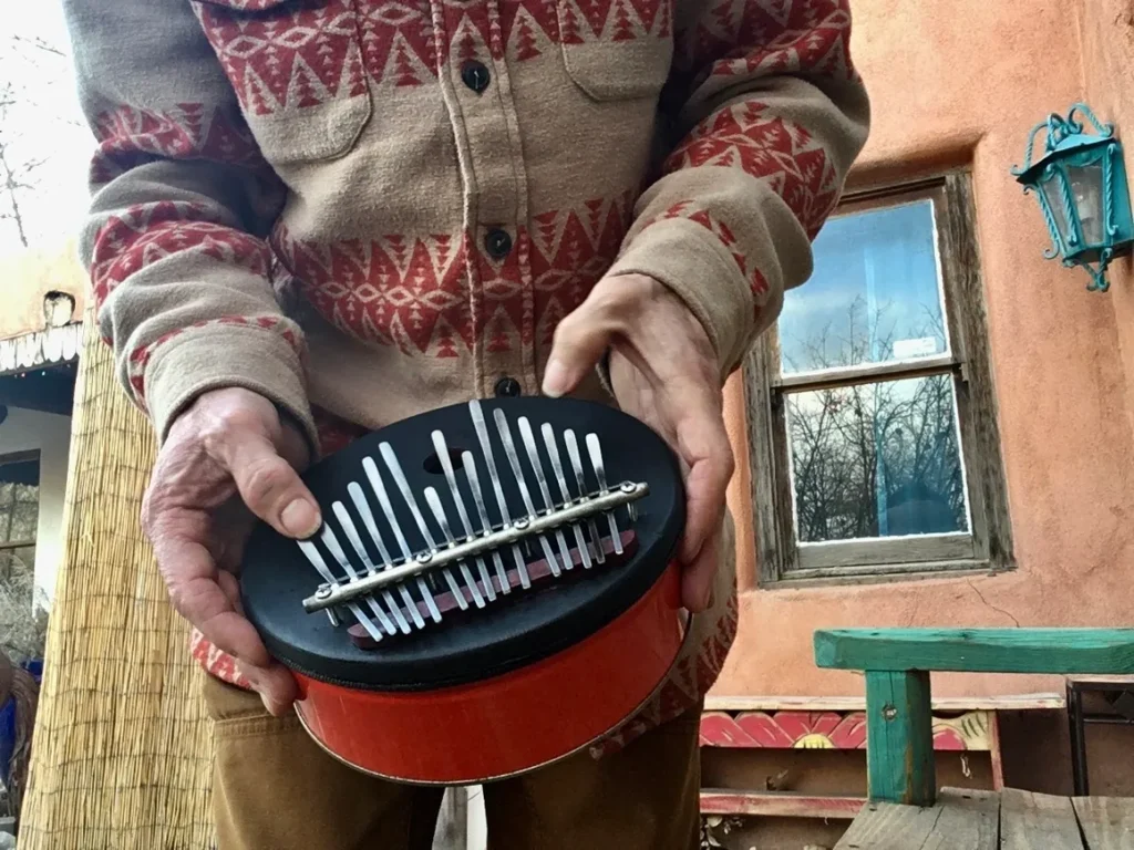 A man is holding a tin can with a metal grater in it, creating unique rhythmic sounds reminiscent of Ngoma, an African music tradition.