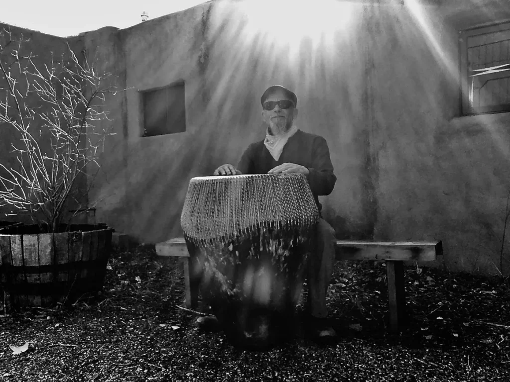 A black and white photo of a man playing a djembe.