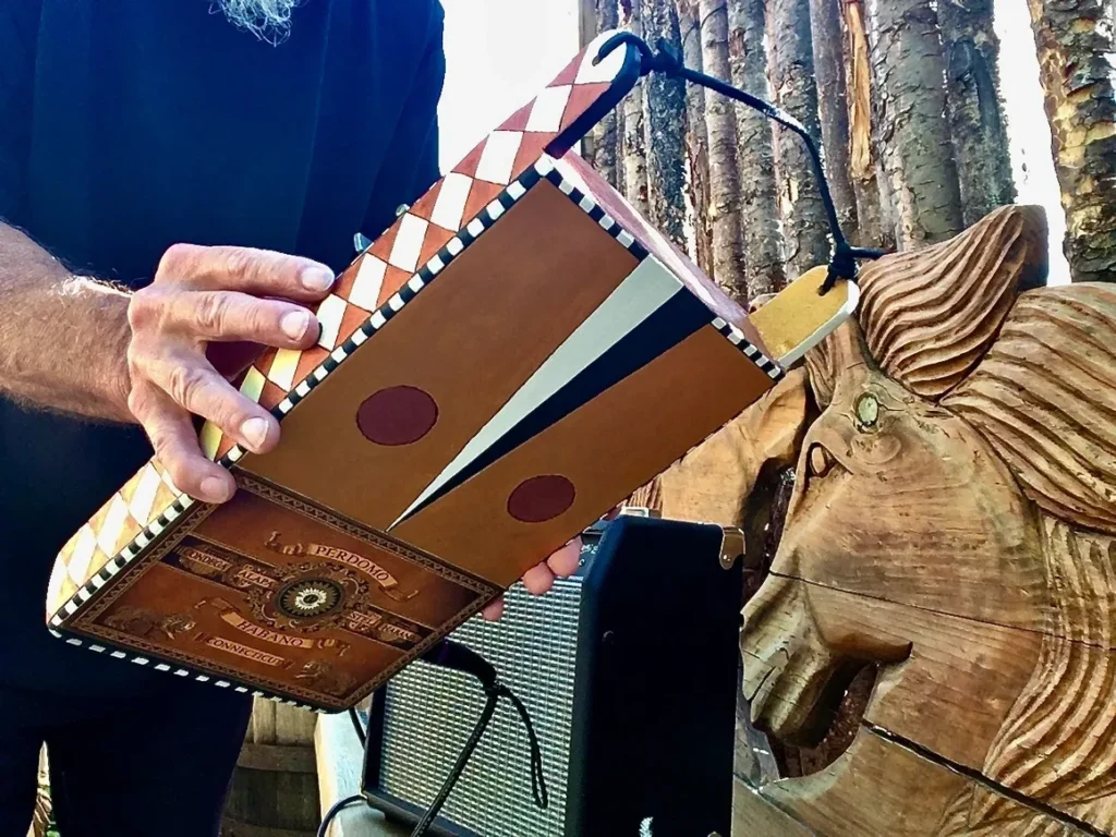 A man holding a wooden box, resembling a Lamellaphone instrument, in front of a tree.