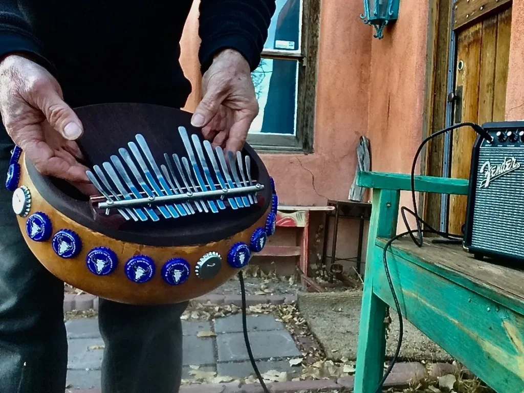 A man is playing an African harp instrument, the Ilimba, on a bench.