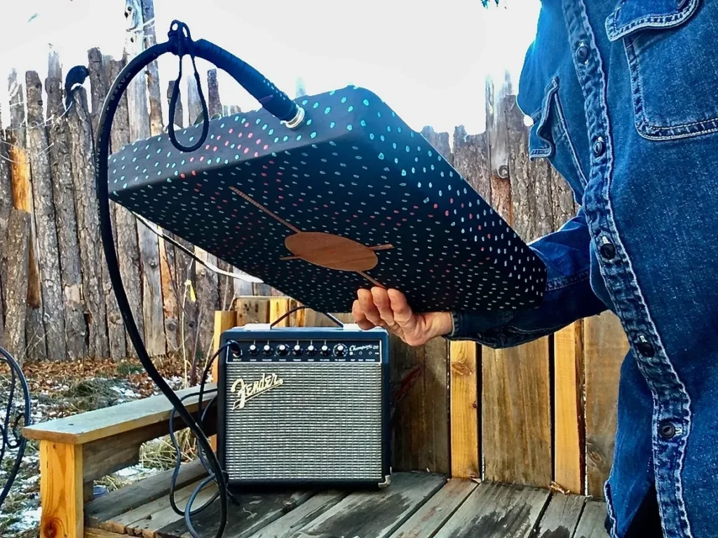 A man is holding a box with a guitar, specifically a Kongoma, in it.