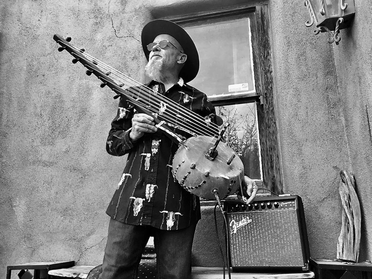 A man in a hat playing Ngoma, an African musical instrument, in front of a house.