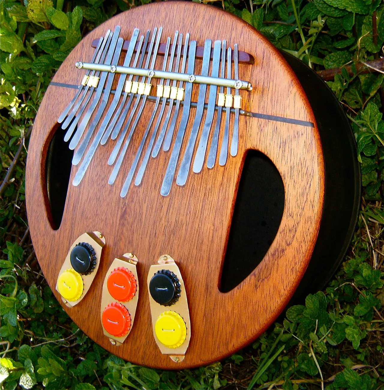 A wooden ukulele, resembling African harps, is sitting in the grass.