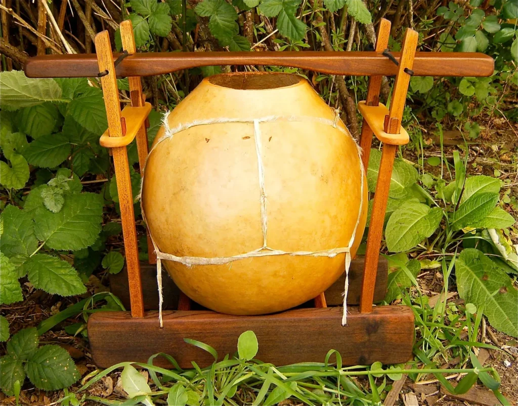 A large pot, resembling a gourd instrument, sitting on a wooden stand in the grass.