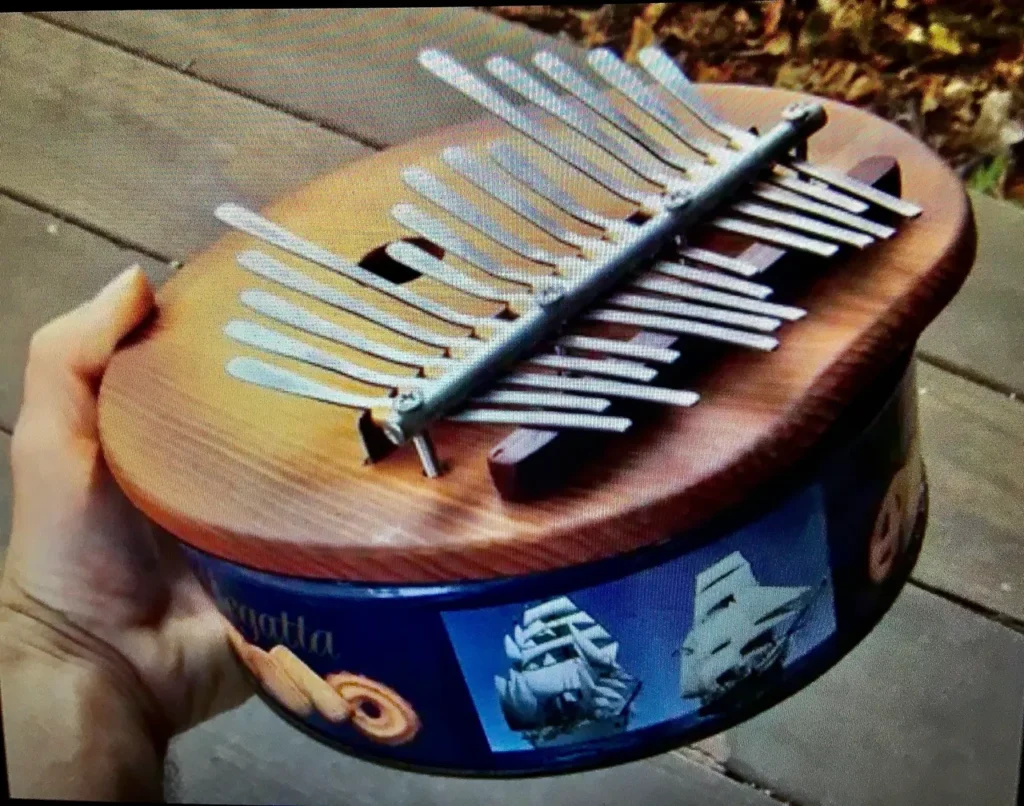 A person holding a tin box with a musical instrument called Ngoma inside.