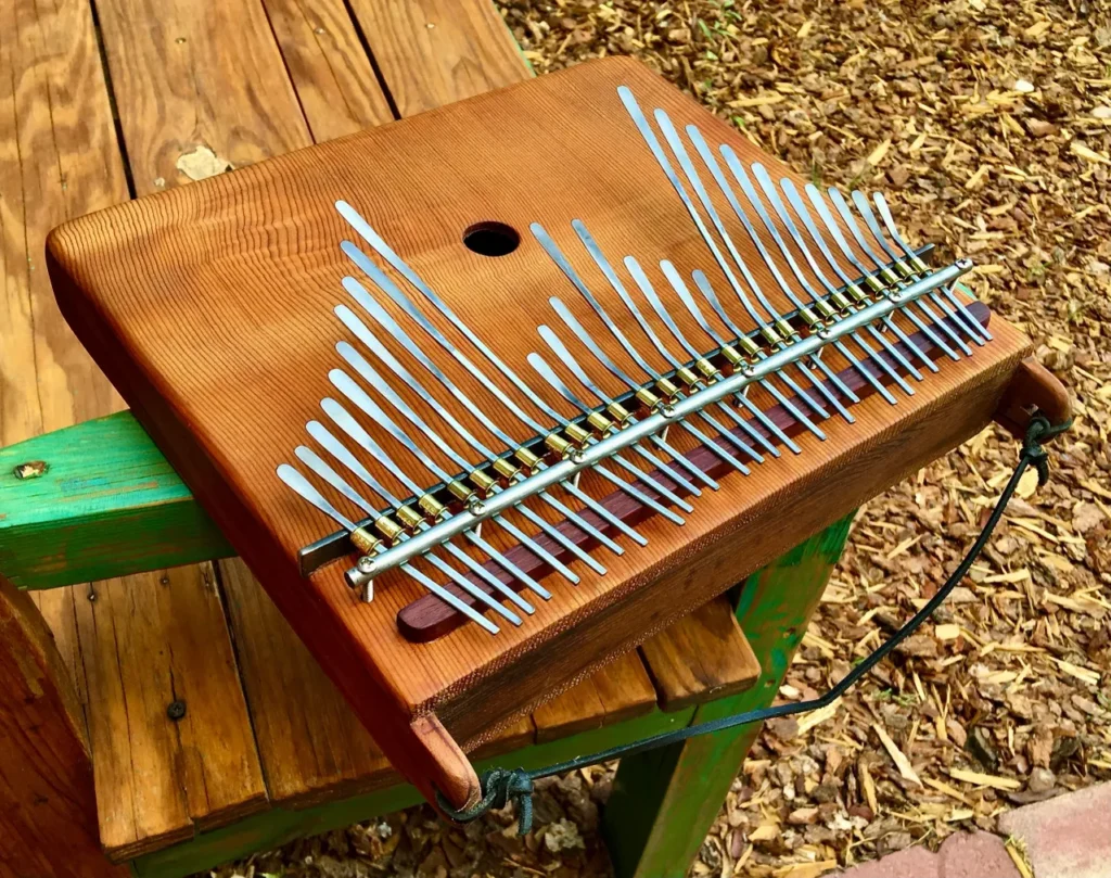 A wooden Marimbula with metal tines sitting on top of a wooden bench.