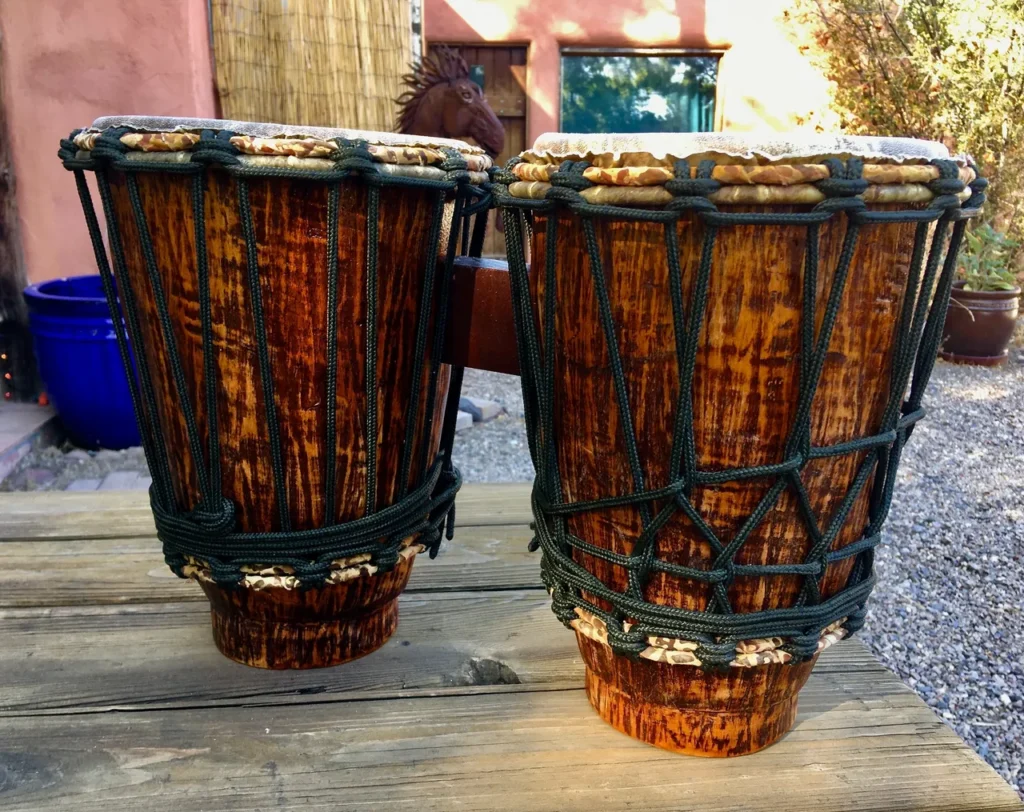 Two wooden djembes, traditional African drums, sitting on a wooden table.