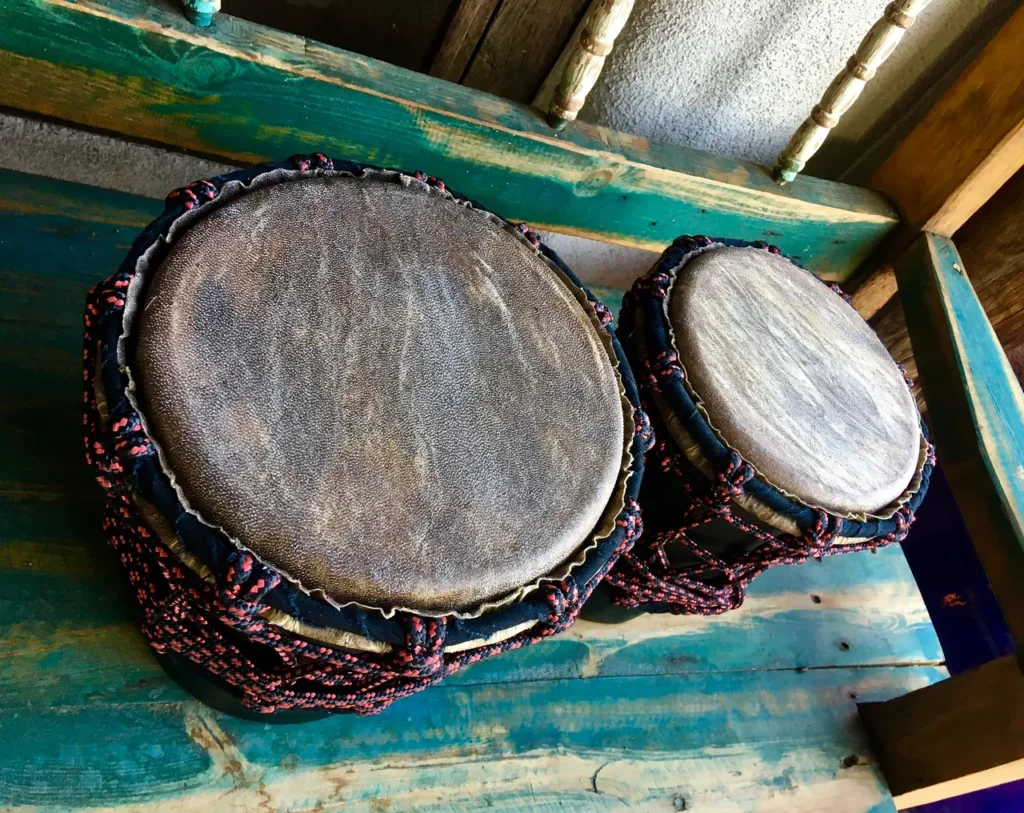 Two djembe drums, traditional African percussion instruments, sitting on a wooden bench.