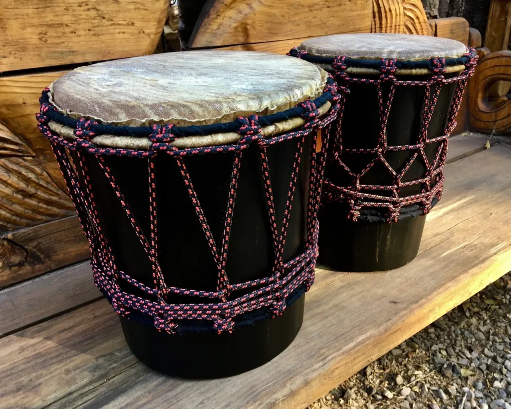 Two djembe drums, commonly found in African cultures, sitting on a wooden bench.