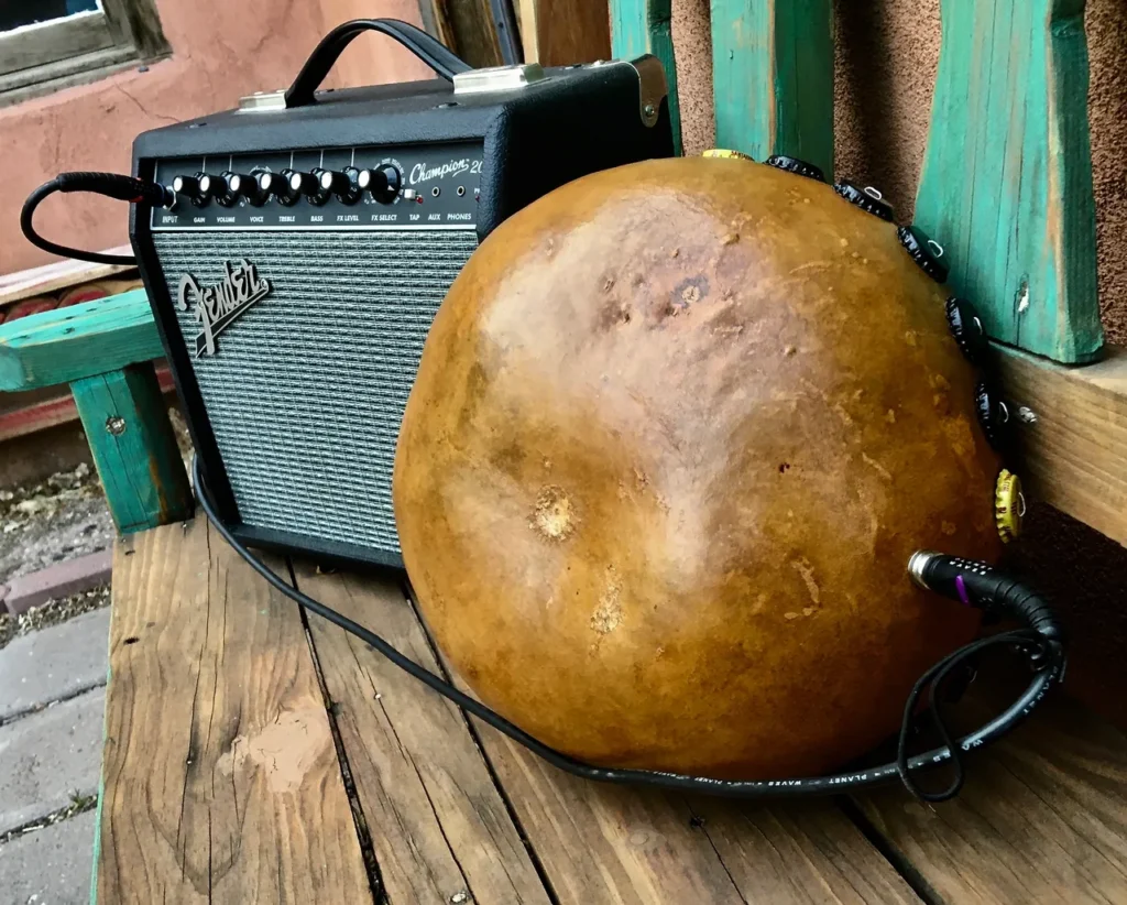 A wooden bench with a guitar and amp next to it, featuring gourd instruments.