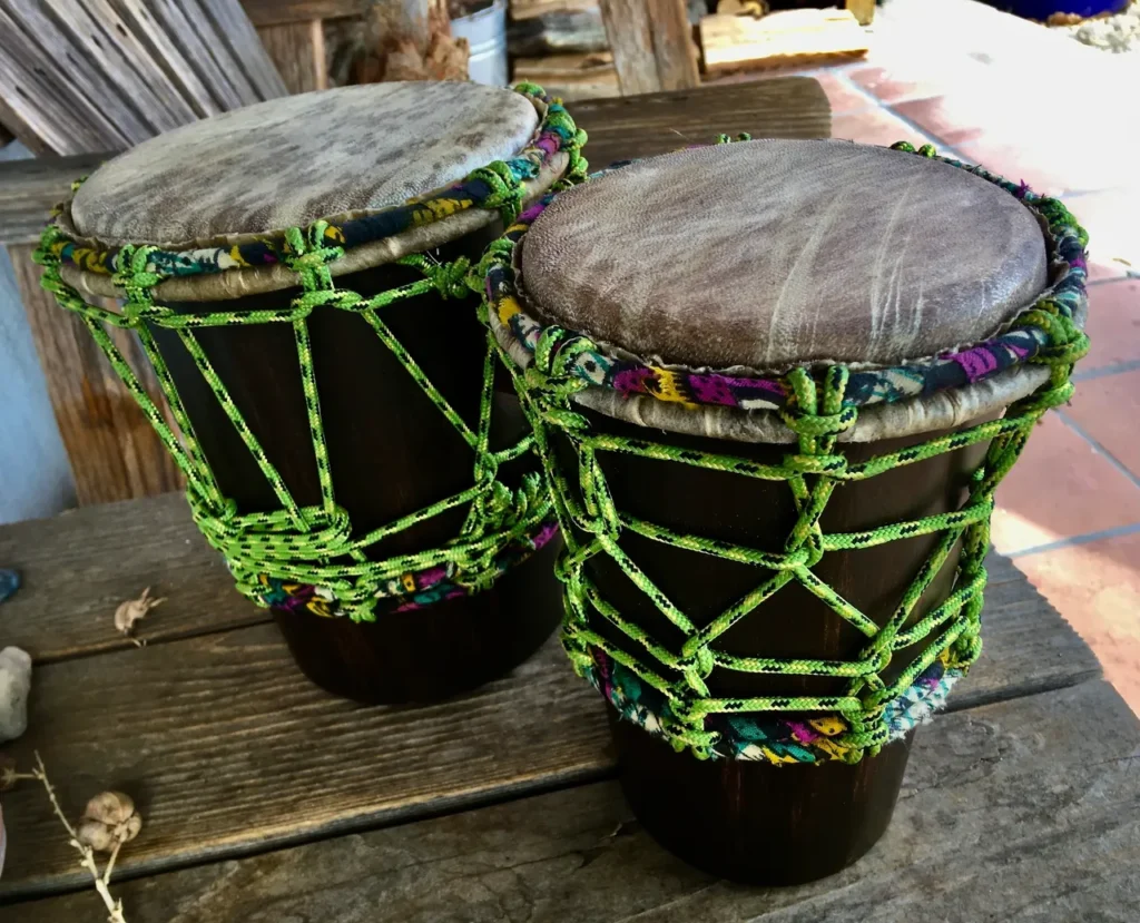 Two djembe drums on a wooden table with an African harp.