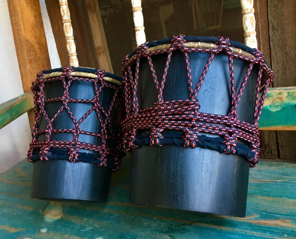 Two black drums, resembling African harps, sitting on a wooden bench.