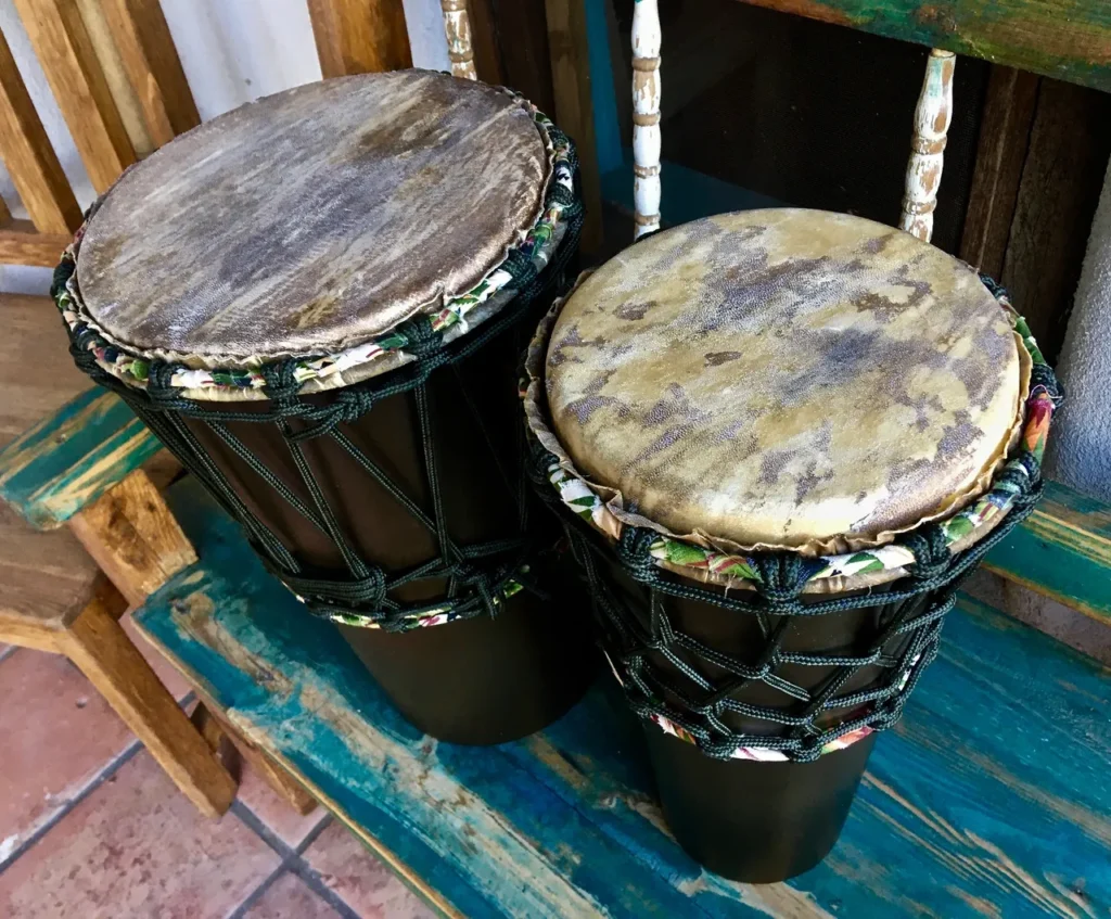 Two djembes, traditional African hand drums, sitting on a wooden bench.