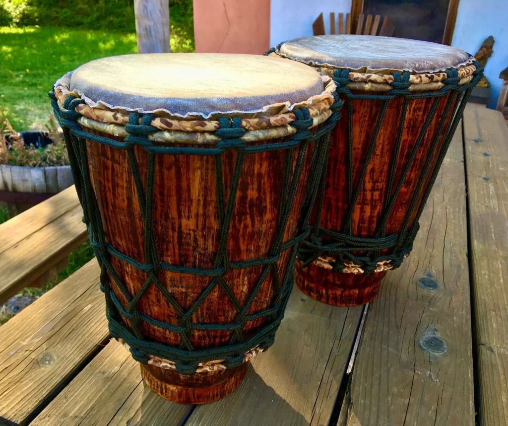 Two wooden djembes, traditional African drums, sitting on a wooden table.