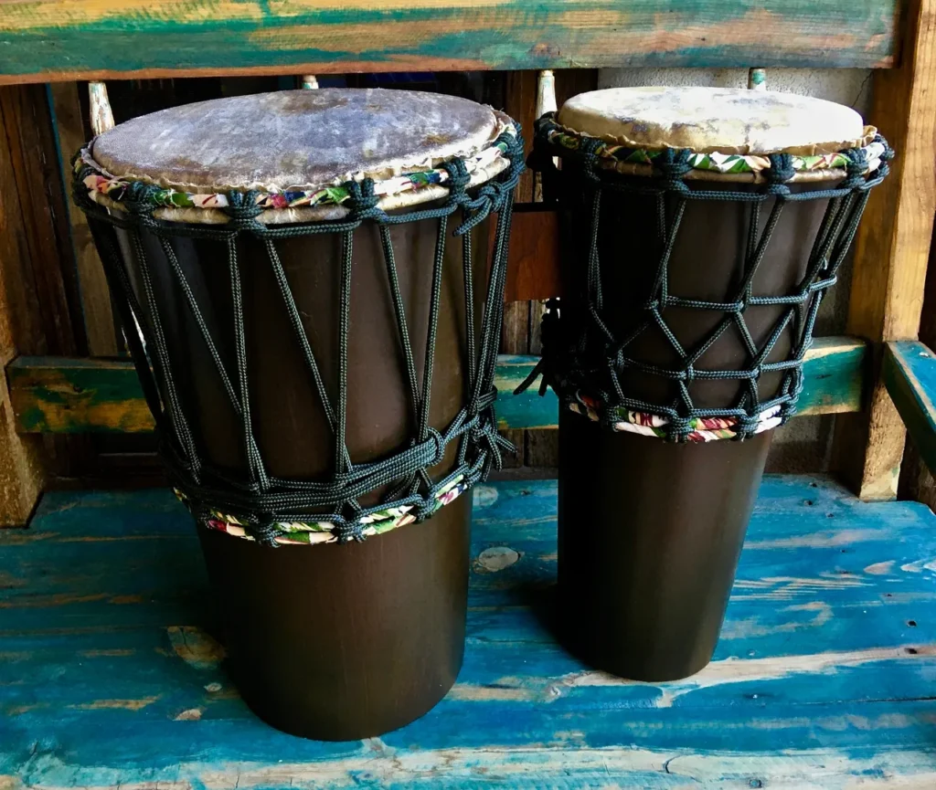 Two djembe drums, African harps, sitting on a wooden bench.