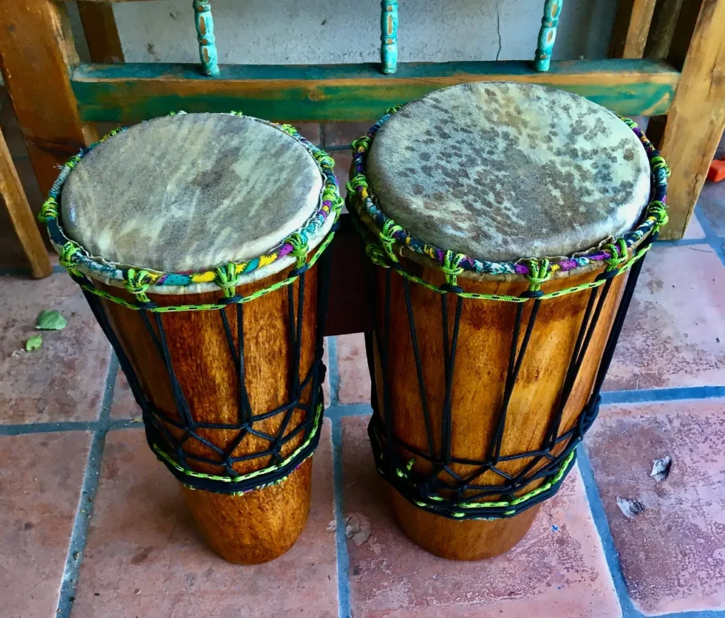 Two wooden djembe drums, commonly used in African music, sitting on a tile floor.