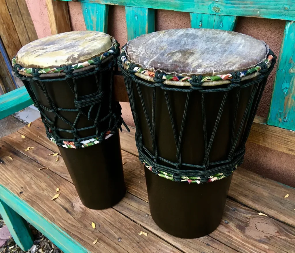 Two djembe drums and an ilimba sitting on a wooden bench.