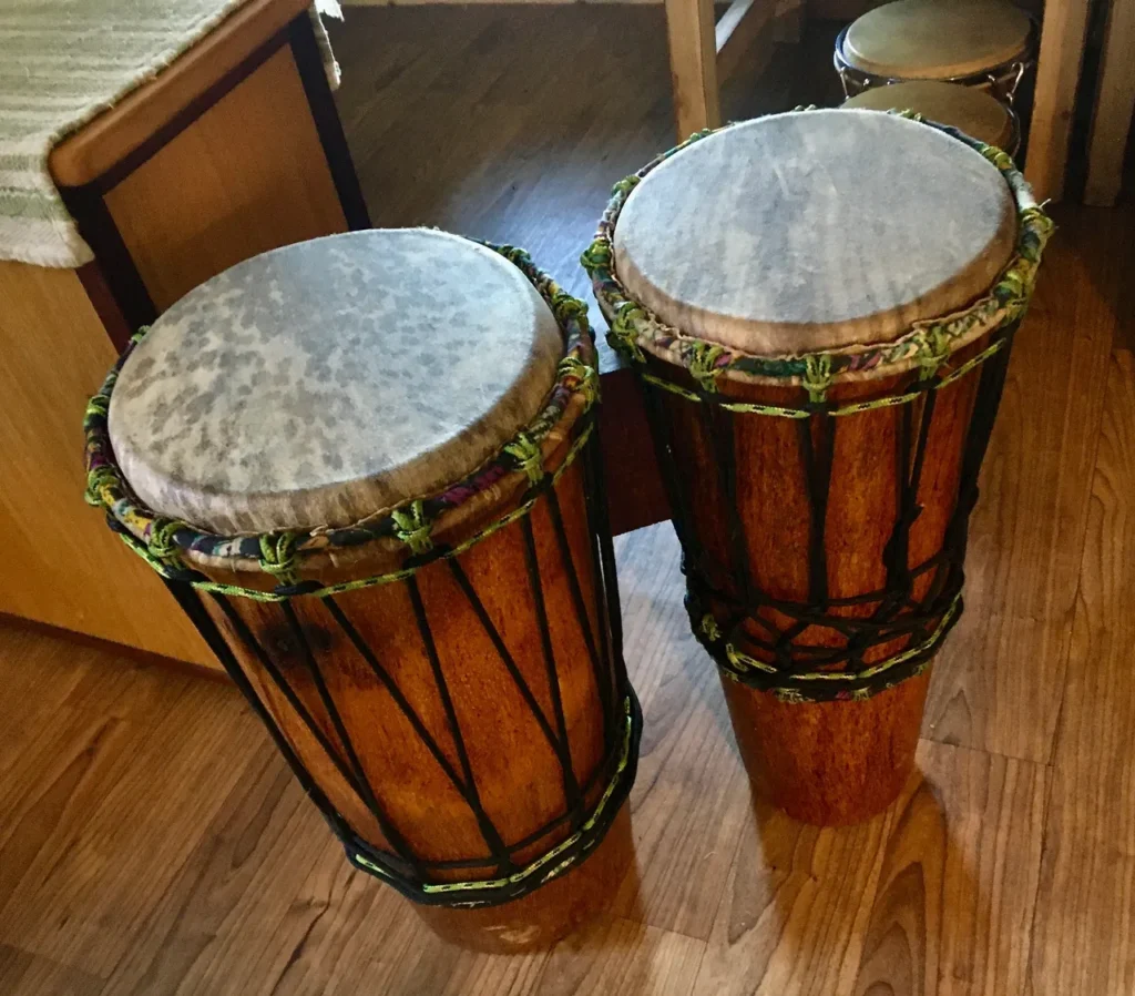 Two djembe drums and an ilimba sitting on a wooden floor.