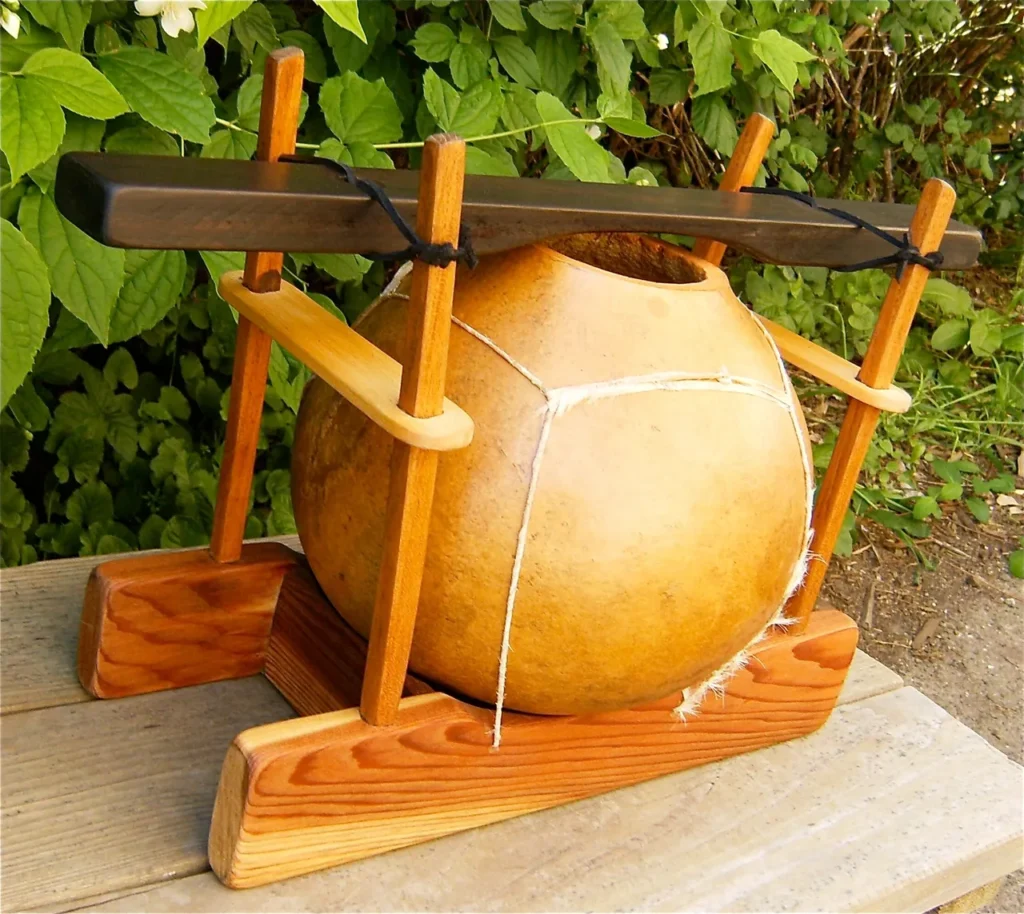 A wooden ball resting on a wooden stand, reminiscent of gourd instruments.