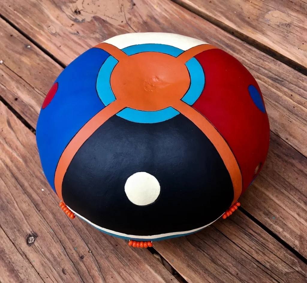 A blue, red, orange, and black ball sitting on a wooden table, surrounded by an Ngoma drum and other African musical instruments.