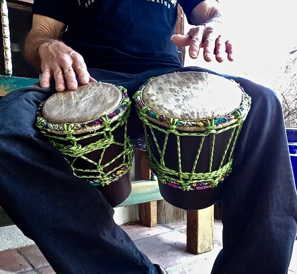 A man sitting on a bench with two djembes and African harps.