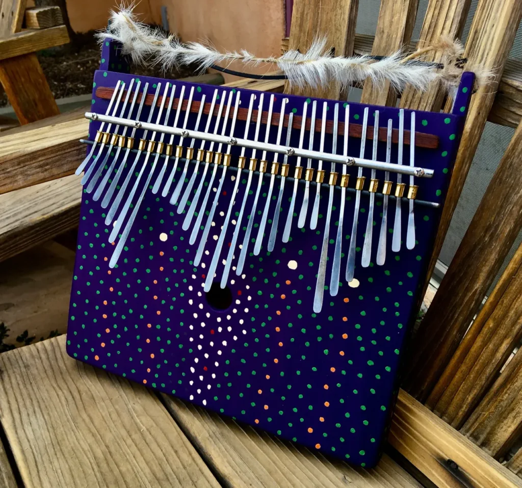 A blue and purple ukulele with feathers sitting on a wooden bench.