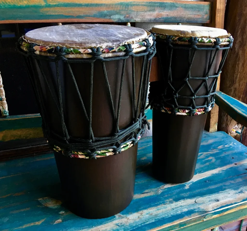 Two djembes, traditional African drums, sitting on a wooden bench.