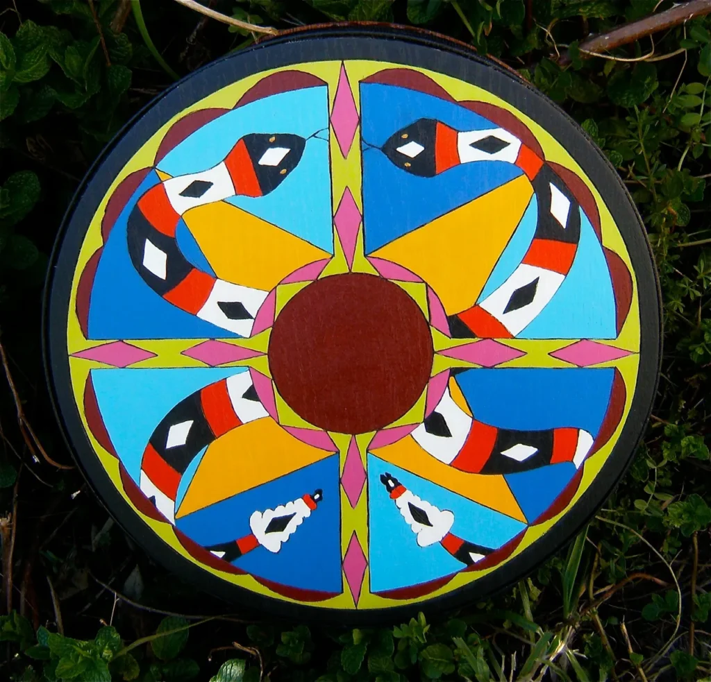 A circular painted Ngoma laying in the grass.