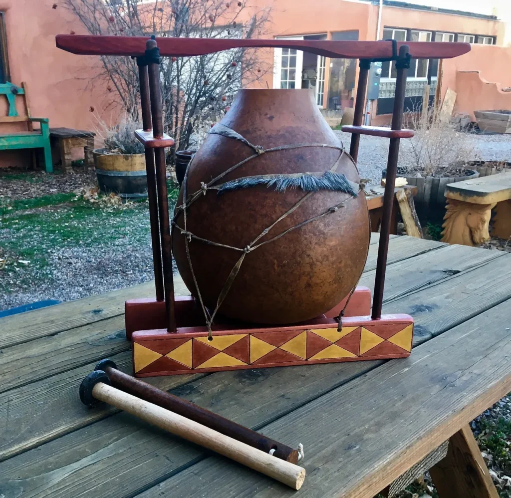 A lamellaphone, resembling a gourd instrument, is sitting on a table next to a wooden stick.