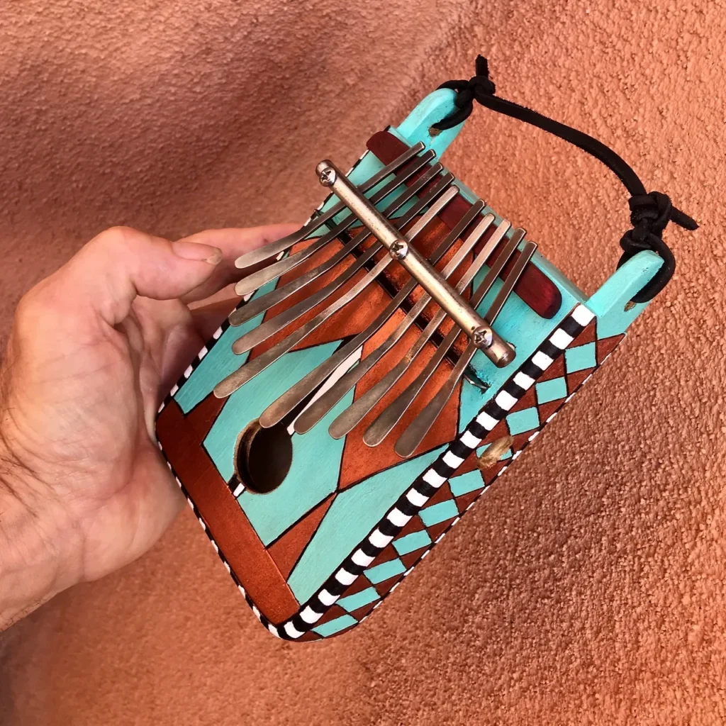 A person playing Ngoma, a traditional African music instrument, while holding a blue and turquoise harmonica.