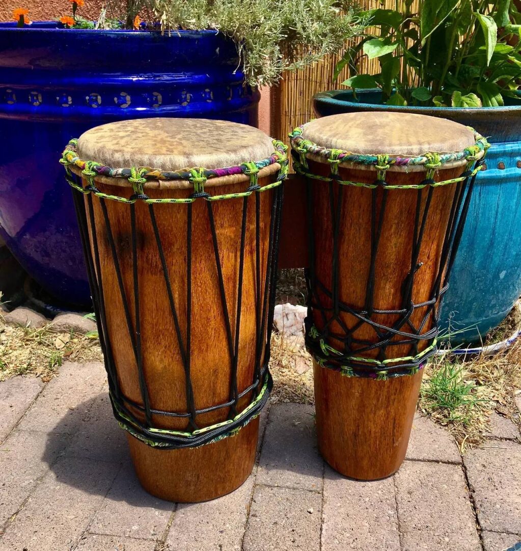 Two wooden djembes, traditional African drums, sitting on a patio.