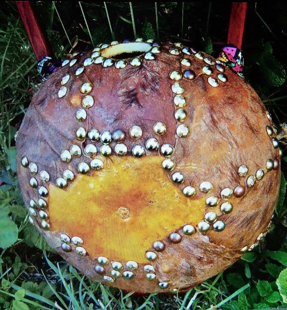 An African drum with studs on it sitting in the grass.