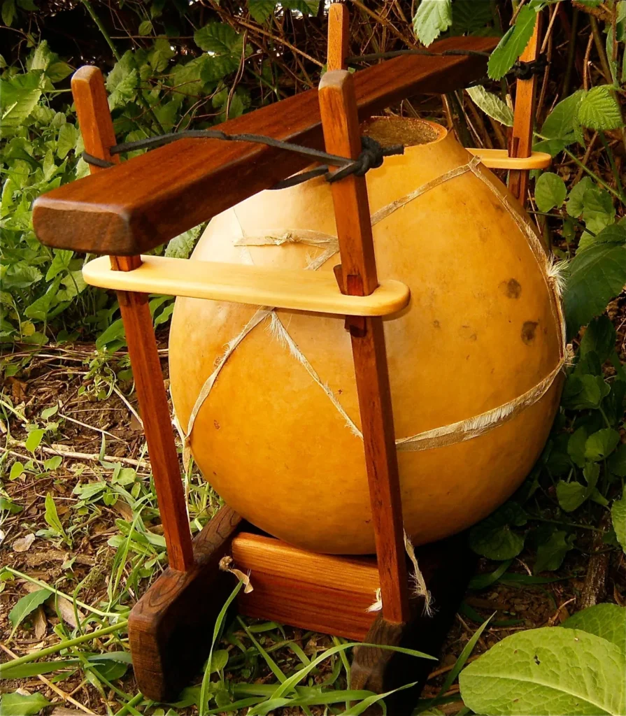 A large yellow ball, resembling a gourd instrument, is sitting on a wooden stand in the grass.