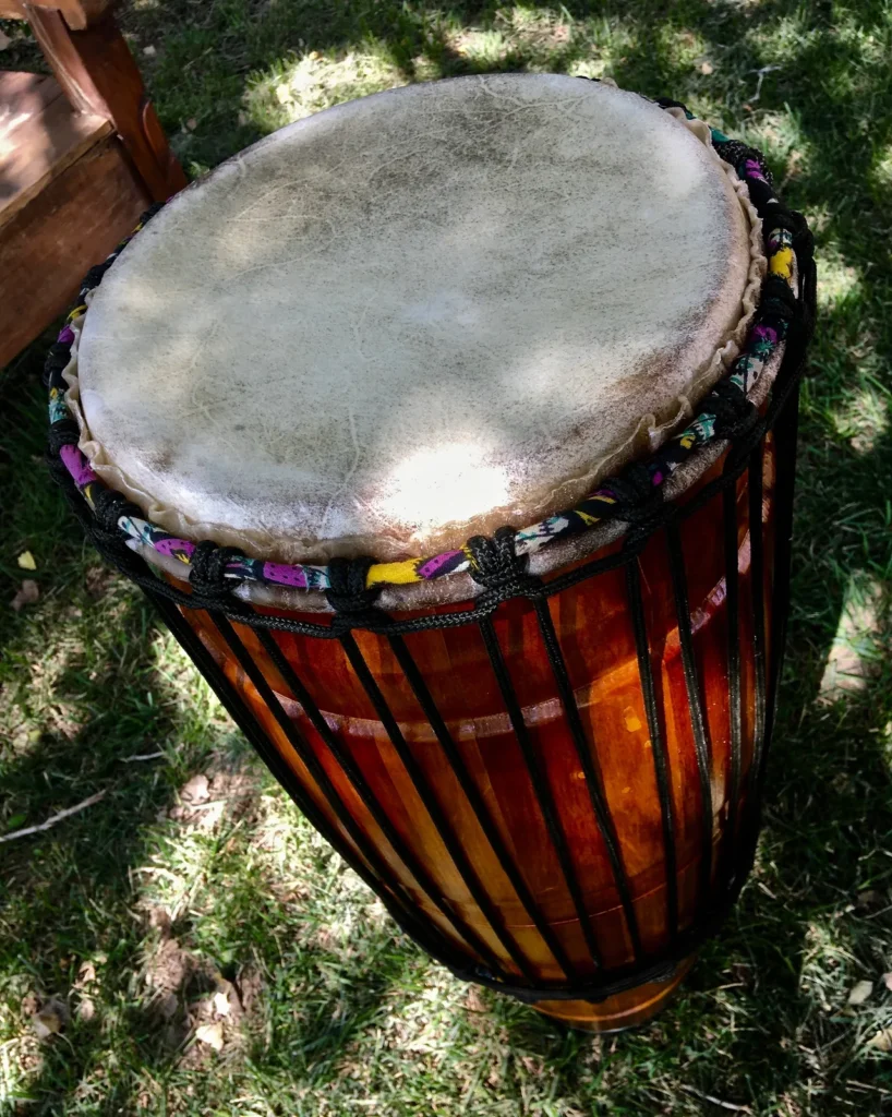 A wooden djembe decorated with Ilimba patterns, sitting on the lush green grass.