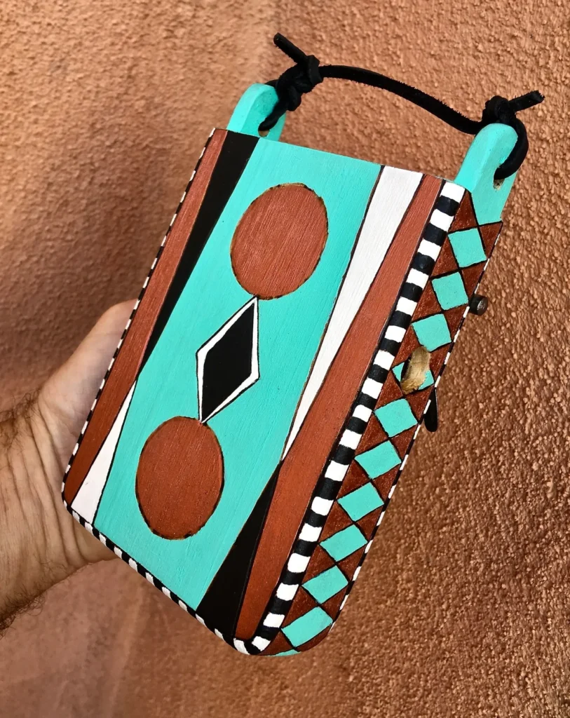 A hand holding a turquoise and black box containing an Ngoma, a traditional African music instrument.